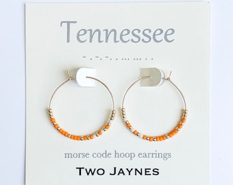 May include: Gold hoop earrings with orange and white beads. The earrings are displayed on a white card with the text "Tennessee" and "morse code hoop earrings TWO JAYNES".