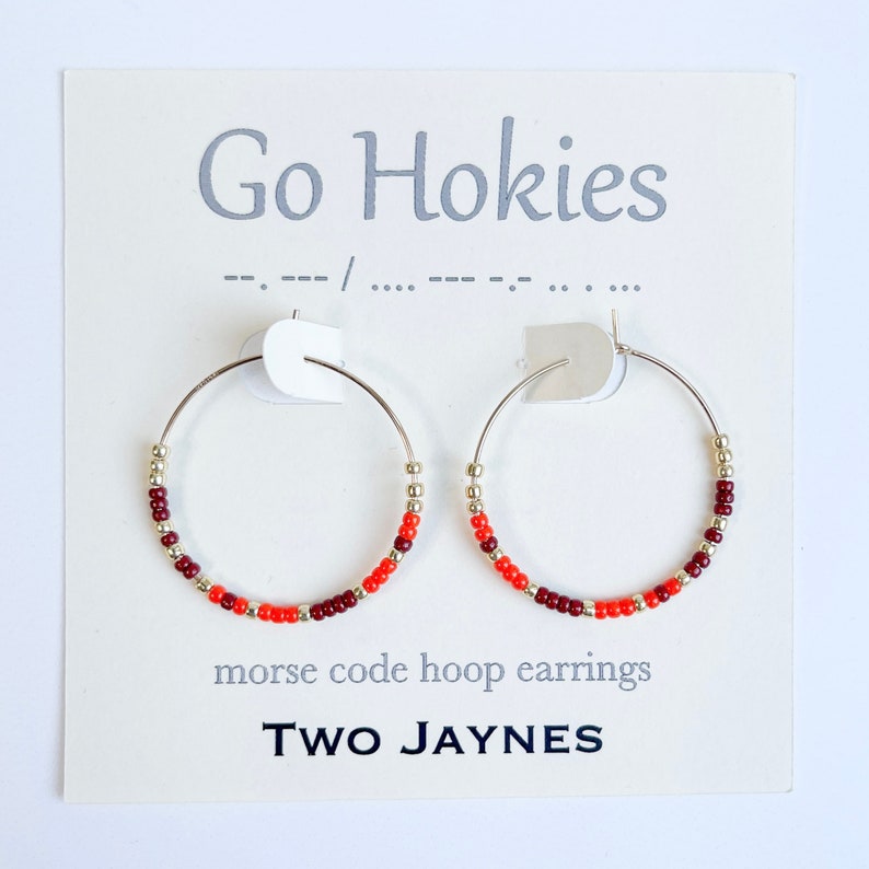 K&ouml;nnte beinhalten: Ein Paar silberne Creolen mit roten, orangefarbenen und goldenen Perlen. Die Ohrringe befinden sich auf einer wei&szlig;en Karte mit dem Text "Go Hokies" und "morse code hoop earrings TWO JAYNES".