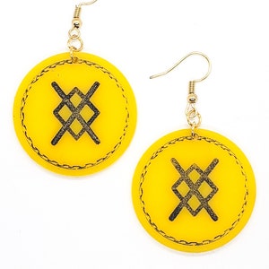 May include: A pair of yellow circular earrings with a black symbol in the center. The earrings have a gold hook.