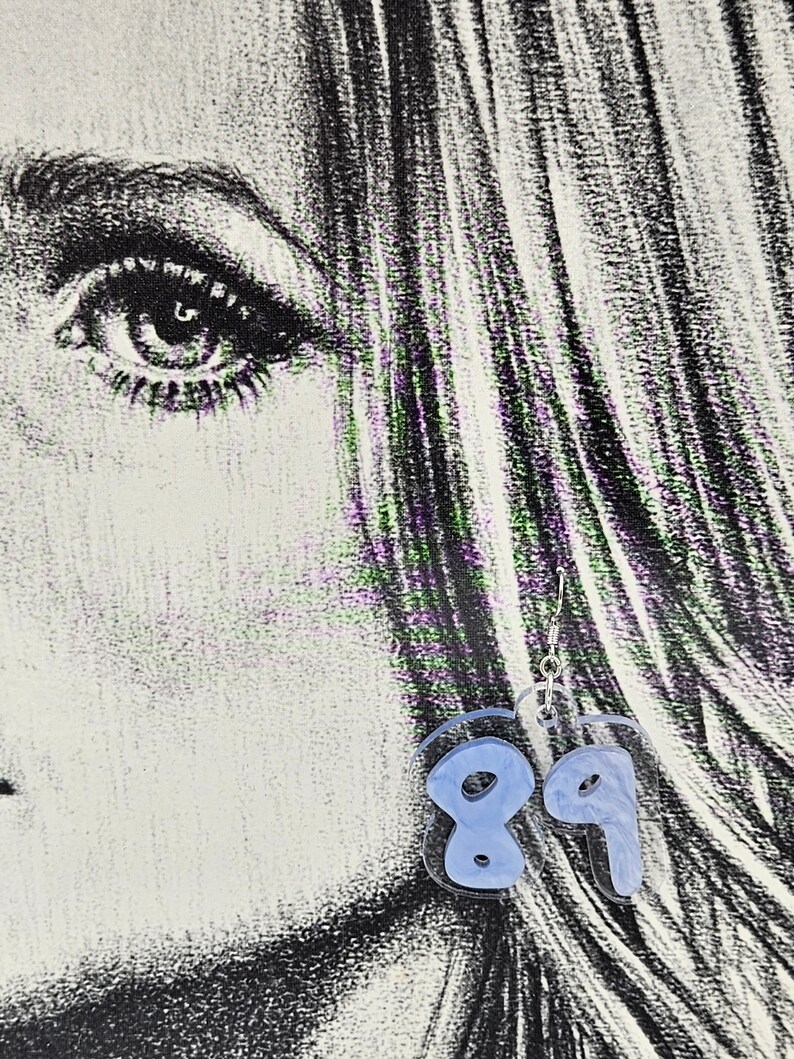 Pu&ograve; includere: Un paio di orecchini in acrilico blu a forma dei numeri 8 e 9. Gli orecchini sono appesi a ganci argentati.