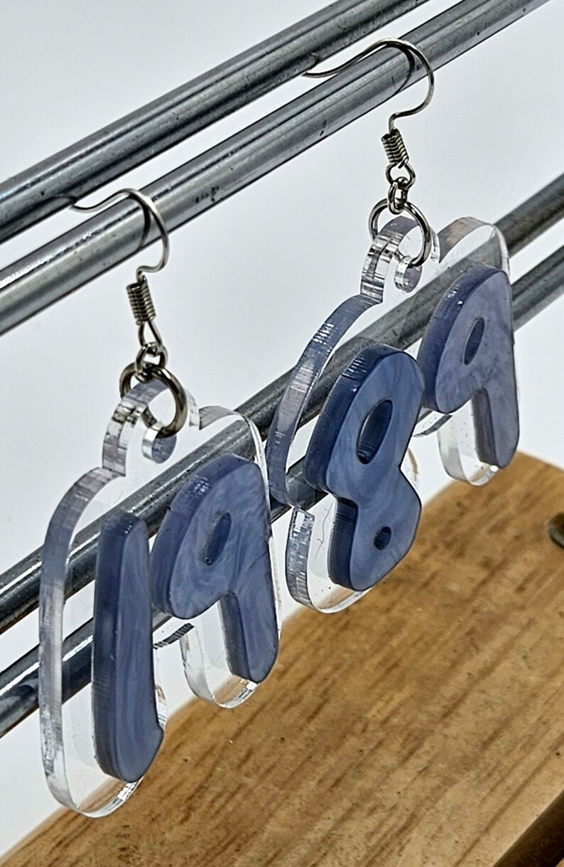 Pu&ograve; includere: Un paio di orecchini in acrilico trasparente con un design a spirale blu. Gli orecchini hanno la forma dei numeri 1999.