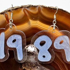 Pu&ograve; includere: Un paio di orecchini in acrilico trasparente con ganci argentati. Gli orecchini hanno la forma dei numeri 1989, con un design a spirale blu chiaro all'interno di ogni numero.
