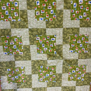 Op de afbeelding: Een groen en wit quilt met een patchwork-ontwerp met een herhalend patroon van kleurrijke insecten en bloemen.