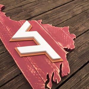 Puede incluir: Un letrero de madera rojo con forma del estado de Virginia con una "F" blanca en el centro. El letrero est&aacute; desgastado y tiene un aspecto r&uacute;stico.