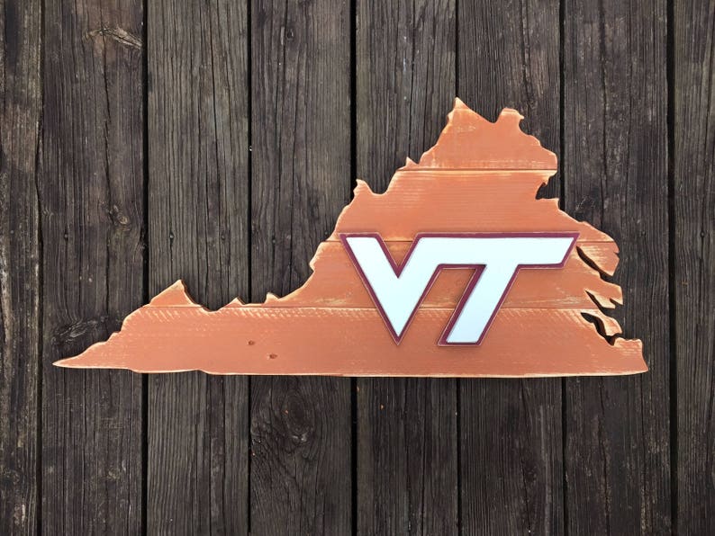 Puede incluir: Un recorte de madera del estado de Virginia pintado en color naranja quemado con un logotipo "VT" blanco en el centro. El logotipo tiene un contorno marr&oacute;n.
