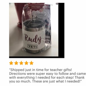 May include: A stainless steel Yeti tumbler with a black lid, personalized with the name "Rudy" in a cursive font. The tumbler is packaged in a clear cellophane bag with a gift tag. The Yeti logo is visible.