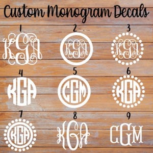 May include: Nine white custom monogram decals in various styles, including circular and ornate designs. The text "Custom Monogram Decals" is at the top. The decals are displayed on a wooden surface.