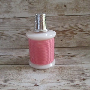 May include: A pink and white glass spool shaped bottle with a silver thimble top.