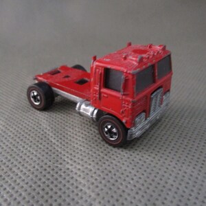 May include: A red toy truck with a flatbed trailer. The truck has a black grill and black wheels. The truck is made of plastic.
