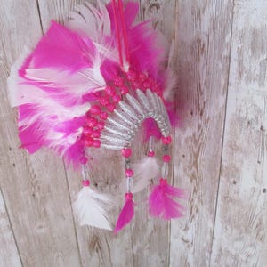 May include: A pink and white feather headdress with silver and pink beads. The headdress is made of feathers and beads and is decorated with a silver band.