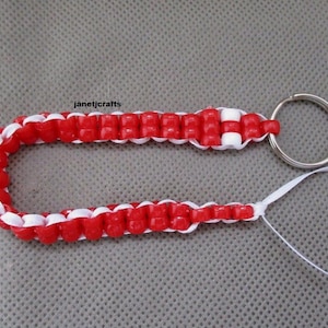 May include: Red and white beaded keychain with a silver key ring. The keychain is made of red and white beads woven together in a pattern. The text "janetjcrafts" is visible in the image.