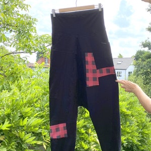 Könnte beinhalten: Schwarze Hose mit rotem und schwarzem Karomuster auf Vorder- und Beinen. Die Hose hängt an einem Kleiderbügel.