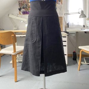 Op de afbeelding: Een zwarte linnen rok met een hoge taille en twee grote zakken aan de voorkant. De rok is geplooid aan de voorkant en heeft een rechte silhouet.