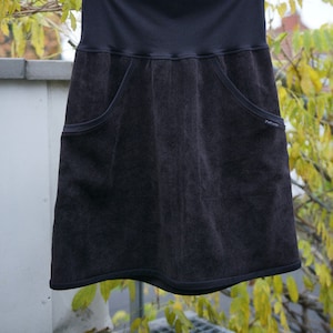 May include: A dark gray skirt with two large pockets on the front. The skirt has a wide waistband and a slightly flared hem.