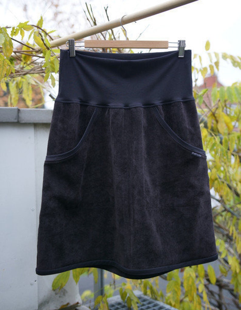 May include: A dark gray skirt with two large pockets on the front. The skirt has a wide waistband and a slightly flared hem.