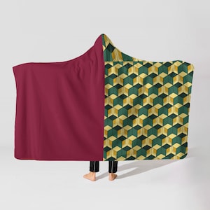 May include: A hooded blanket with a burgundy solid color on the left side and a geometric cube pattern in green, yellow, and black on the right side. The blanket is draped over a person.