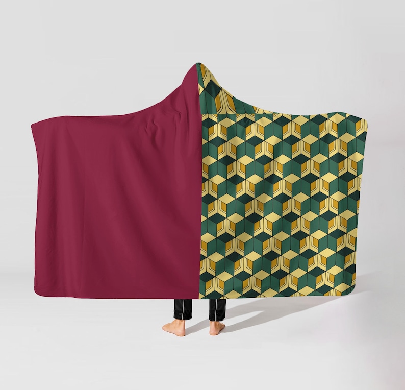 May include: A hooded blanket with a burgundy solid color on the left side and a geometric cube pattern in green, yellow, and black on the right side. The blanket is draped over a person.