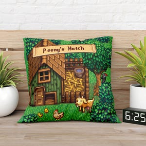 Puede incluir: Un coj&iacute;n decorativo verde con una ilustraci&oacute;n pixelada de un edificio con la etiqueta "Peony's Hutch". El dise&ntilde;o incluye un tejado marr&oacute;n, una puerta de madera y una cabra. Tambi&eacute;n se ven dos plantas en maceta y un reloj digital.