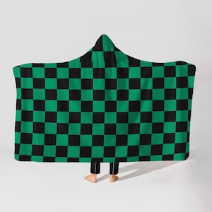 May include: A hooded blanket with a green and black checkered pattern. The blanket is draped over a person, with the hood up. The blanket is made of a soft material and is designed to be worn.