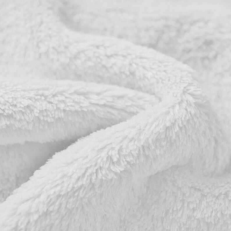 May include: Close-up of a white, fluffy, and soft blanket. The fabric has a plush texture with visible fibers and folds, creating a sense of warmth and comfort. The blanket appears to be made of a soft material.