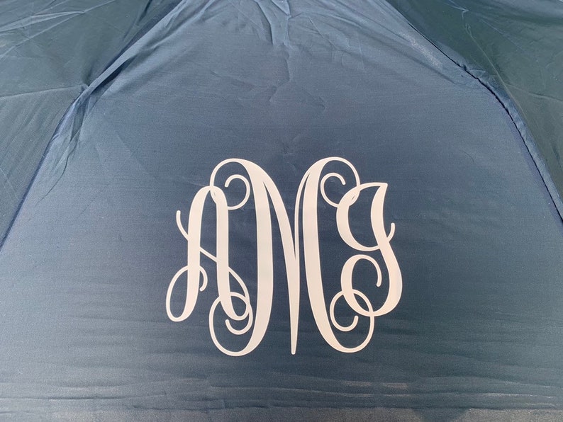 May include: A navy blue umbrella with a white monogram of the letters "A M G" in a script font.