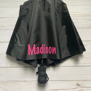 May include: Black umbrella with a pink personalized name "Madison" printed on the canopy.