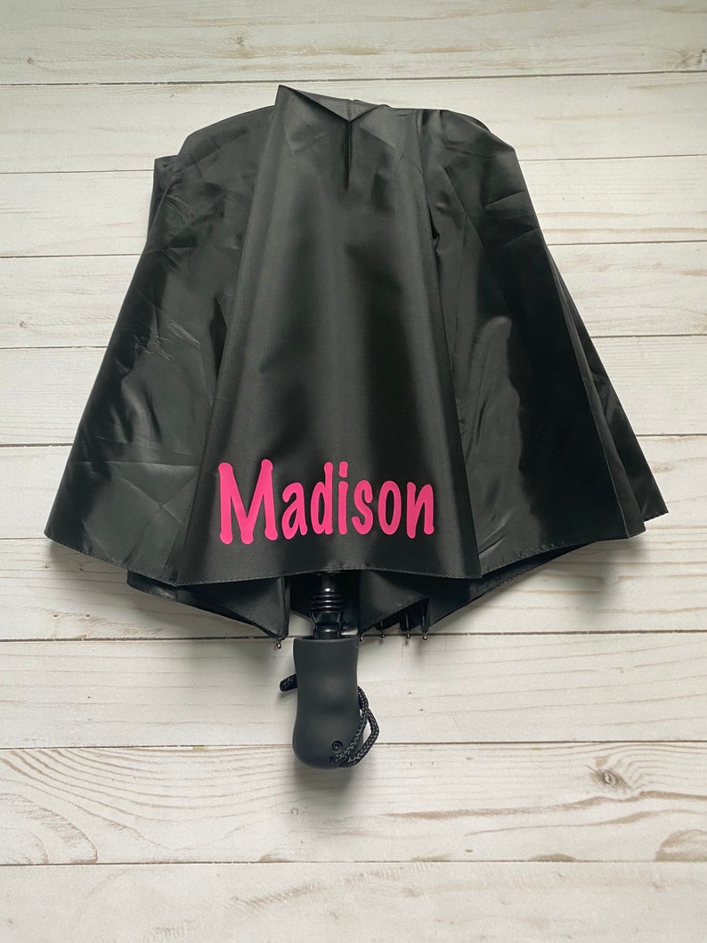 May include: Black umbrella with a pink personalized name "Madison" printed on the canopy.
