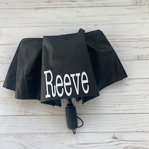 May include: Black umbrella with a white personalized name "Reeve" printed on the canopy.