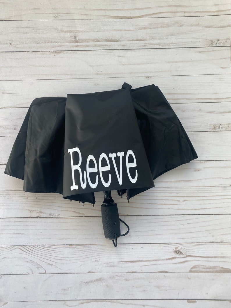 May include: Black umbrella with a white personalized name "Reeve" printed on the canopy.