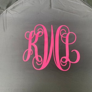 May include: A black umbrella with a pink monogram of the letters "KWL" in a cursive font.