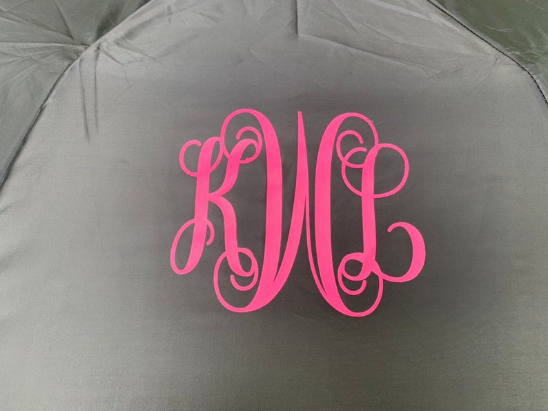 May include: A black umbrella with a pink monogram of the letters "KWL" in a cursive font.
