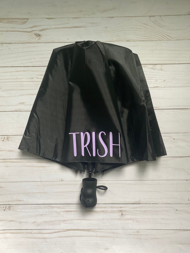 May include: A black umbrella with a purple inscription that reads "TRISH".