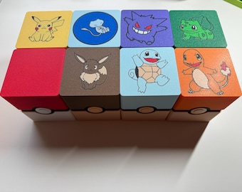 Può includere: Otto scatole cubiche colorate con disegni di personaggi Pokémon. Ogni cubo presenta un personaggio diverso, tra cui Pikachu, Gengar e Squirtle. Le scatole sono impilate, creando un display visivamente accattivante.