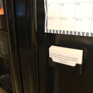 May include: A black refrigerator with a calendar and a card holder with a white card that reads "Fear not, Kendall, for I have redeemed you: I have called you by name, Kendall, you are mine." Isaiah 43:1