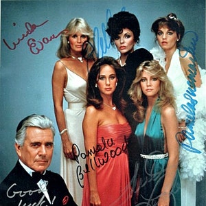 Puede incluir: Un grupo de seis personas, incluyendo cinco mujeres y un hombre, están posando para una foto. Las mujeres visten atuendos formales, incluyendo vestidos largos de varios colores. El hombre lleva un esmoquin negro. La foto está firmada por las seis personas, incluyendo los nombres "Linda Evans", "Pamela Bellwood" y "Farrah Fawcett".