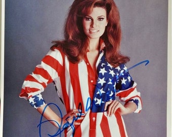 May include: A woman wearing a red, white, and blue shirt with stars and stripes. The shirt is unbuttoned and the woman is posing with her hand on her hip. The woman has long, red hair and is smiling. The image is signed by the woman.