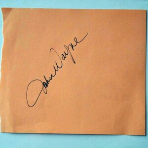 Peut inclure: Un gros plan sur une signature manuscrite sur un papier orange clair. La signature est "John Wayne".