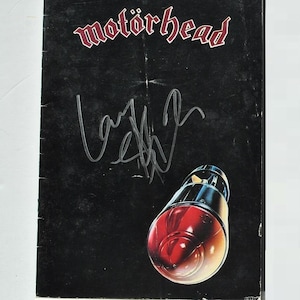 May include: A black album cover featuring the band name "Motörhead" in red and white lettering. The cover includes an image of a red and chrome object, and an autograph. The album cover is slightly worn.