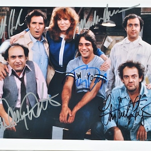 Może przedstawiać: Czarno-białe zdjęcie pięciu osób, wszystkie uśmiechnięte. Osoby stoją przed ceglaną ścianą z tabliczką z napisem „Myjnia samochodowa” w tle. Zdjęcie jest podpisane przez wszystkie pięć osób.