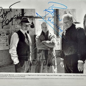 May include: Black and white photo of three men in a boxing gym. The men are standing in front of a boxing bag and a poster that says "Boxing The Odeum". The men are all wearing jackets and have their arms crossed. The photo is signed by the three men: Robert Loggia, Brian Dennehy, and James Marshall.