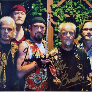 Puede incluir: Un grupo de cinco hombres con camisas coloridas y estampados florales posan para una foto. Todos sonríen y miran a la cámara. El hombre del centro sostiene una flauta plateada. Los hombres han firmado sus nombres en la foto.