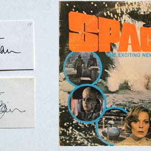 May include: An image featuring two signed cards and a vintage magazine cover. The magazine cover has the title "SPACE 1999" in orange and white, with images of actors and scenes from the series. The cards have handwritten signatures.