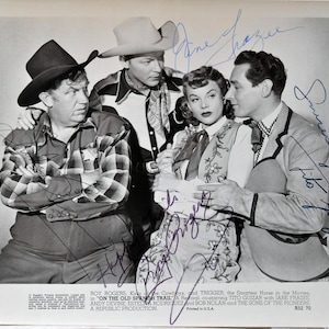 May include: Black and white photo of four actors in Western wear, including Roy Rogers, Trigger the horse, and Jane Frazee. The photo is signed by all four actors. The text on the photo reads "Roy Rogers, King of the Cowboys, and Trigger the Smartest Horse in the Movies, in "On the Old Spanish Trail" A Revival, co-starring Tito Guizar with Jane Frazee, Andy Devine, Estela Rodriguez and Bob Nolan and The Sons of the Pioneers, A Republic Production."