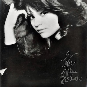 May include: A monochrome photograph of a woman with dark hair, gazing towards the camera. The image features a handwritten signature and the word "Love".