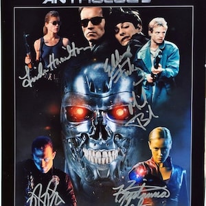 May include: A movie poster for "The Terminator Anthology" featuring Arnold Schwarzenegger and other cast members. The poster has signatures and a metallic skull with glowing red eyes. The text "The Terminator Anthology" is at the top.