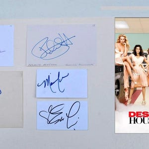 Puede incluir: Imagen con tarjetas autografiadas y un póster de Desperate Housewives. Las tarjetas muestran firmas en tinta azul. El póster muestra el elenco de la serie en una lavandería, con el título en rojo y blanco.