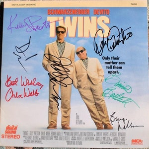Może przedstawiać: Okładka kasety VHS do filmu "Bliźniacy" z Arnoldem Schwarzeneggerem i Danny DeVito. Okładka przedstawia niebieskie niebo w tle z tytułem "Bliźniacy" w dużych białych literach. Aktorzy są przedstawieni w centrum okładki, Schwarzenegger po lewej, a DeVito po prawej. Okładka zawiera również slogan "Tylko ich matka może ich odróżnić."