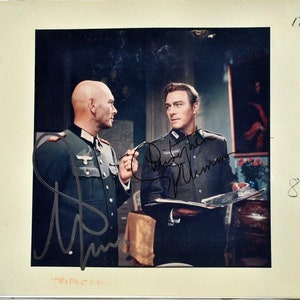 May include: A black and white photo of two men in military uniforms. The man on the left is holding a cigarette and the man on the right is holding a book. The photo is signed by both men. The man on the left's signature is "Dieter", and the man on the right's signature is "Dietrich" followed by an illegible signature.