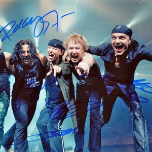 May include: A signed photograph of a rock band with five members. The band members are wearing casual clothing and are posing for the camera. The photograph is signed by all five members of the band.