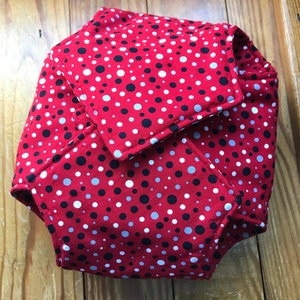 May include: Red fabric with black, white, and gray polka dots. The fabric is folded into a geometric shape.